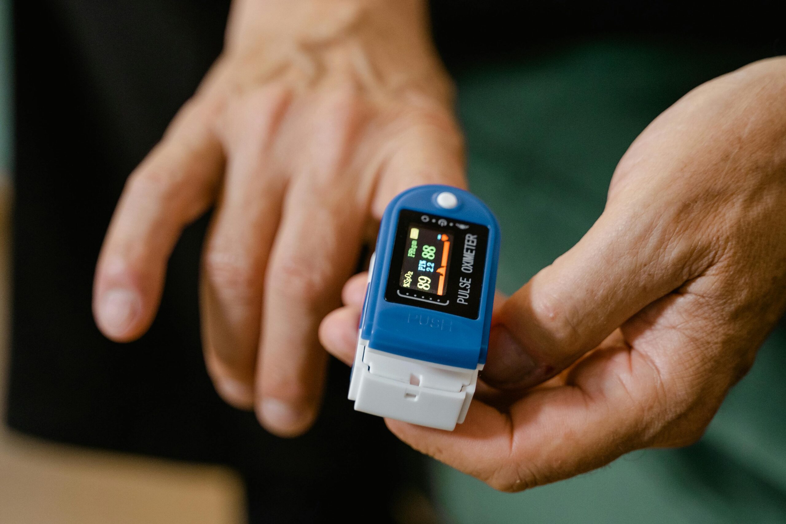 Close-up of a hand holding a blue pulse oximeter measuring oxygen levels and pulse rate.